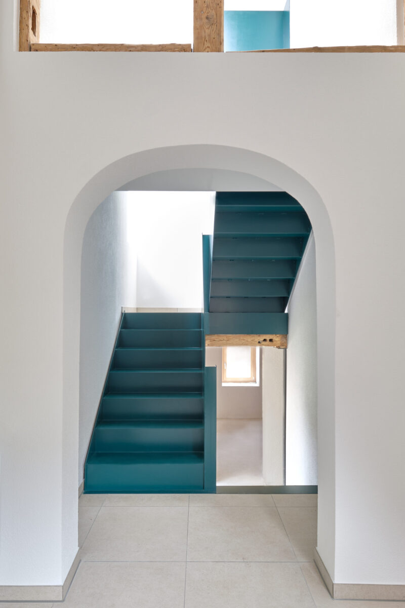 sanierung wohnhaus – treppenaufgang mit gefalteter stahltreppe treppe mit sichtbetonwand und türkis lackierten stufen