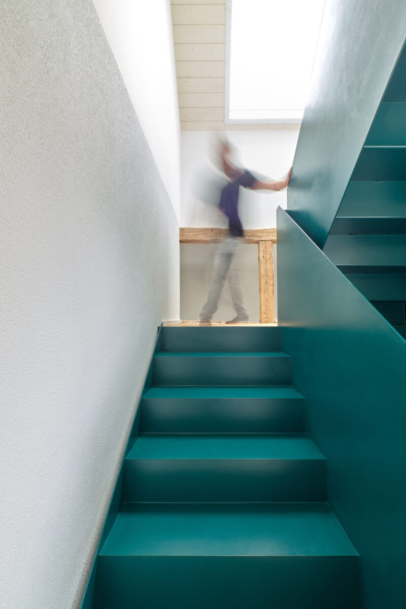 sanierung wohnhaus – treppenaufgang petrol türkise treppe im sanierten wohnhaus mit person im hintergrund
