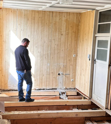 Mann steht auf dem Boden eines Raumes mit freiliegenden Dielen und Holzverkleidung an den Wänden.