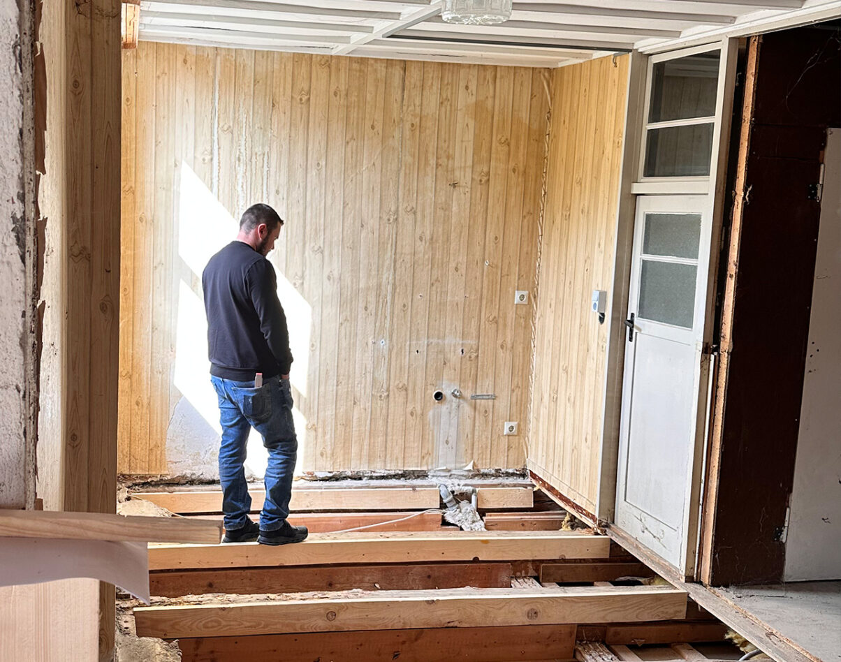 ausbau dachgeschoss mühle dietfurt – nachhaltige sanierung und umnutzung Mann steht auf dem Boden eines Raumes mit freiliegenden Dielen und Holzverkleidung an den Wänden.
